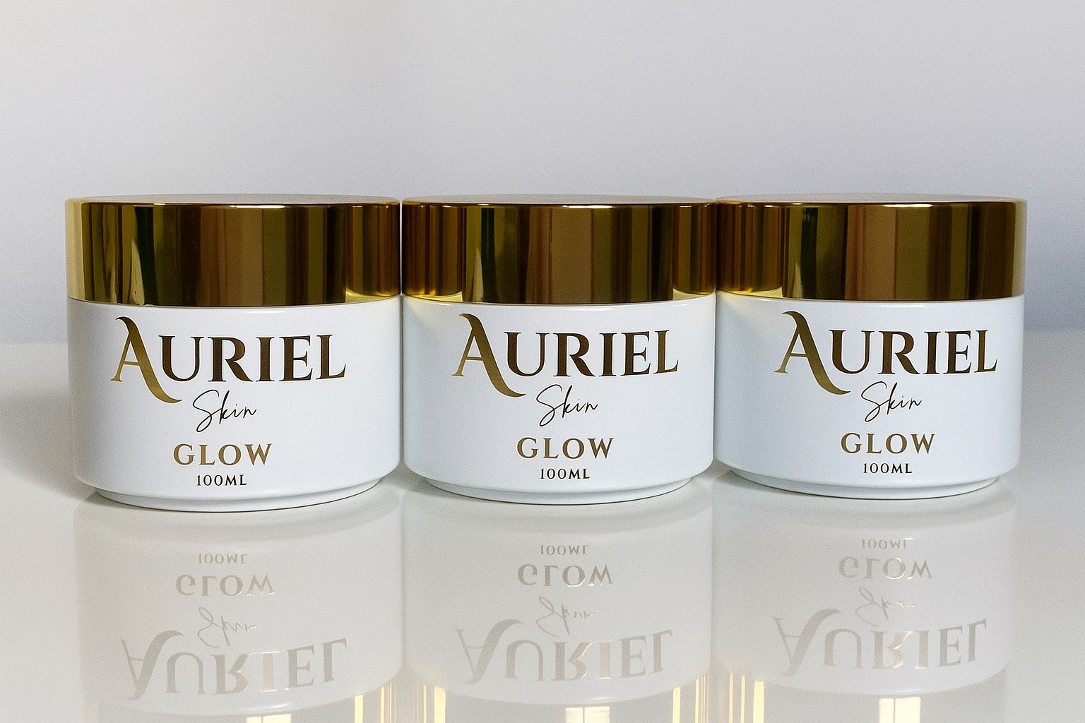 Three jars of Auriel Skin Glow cream on a reflective surface with a white background